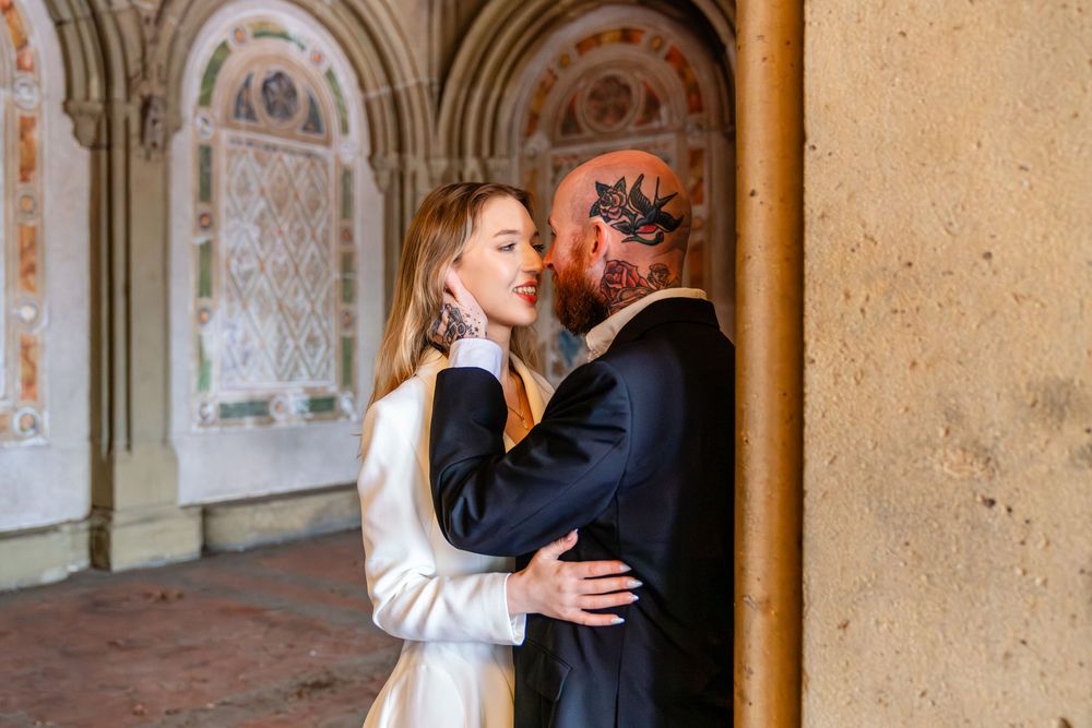 Couple embracing at Bethesda Terrace in Central Park, man with face tattoos in suit, woman in white dress.