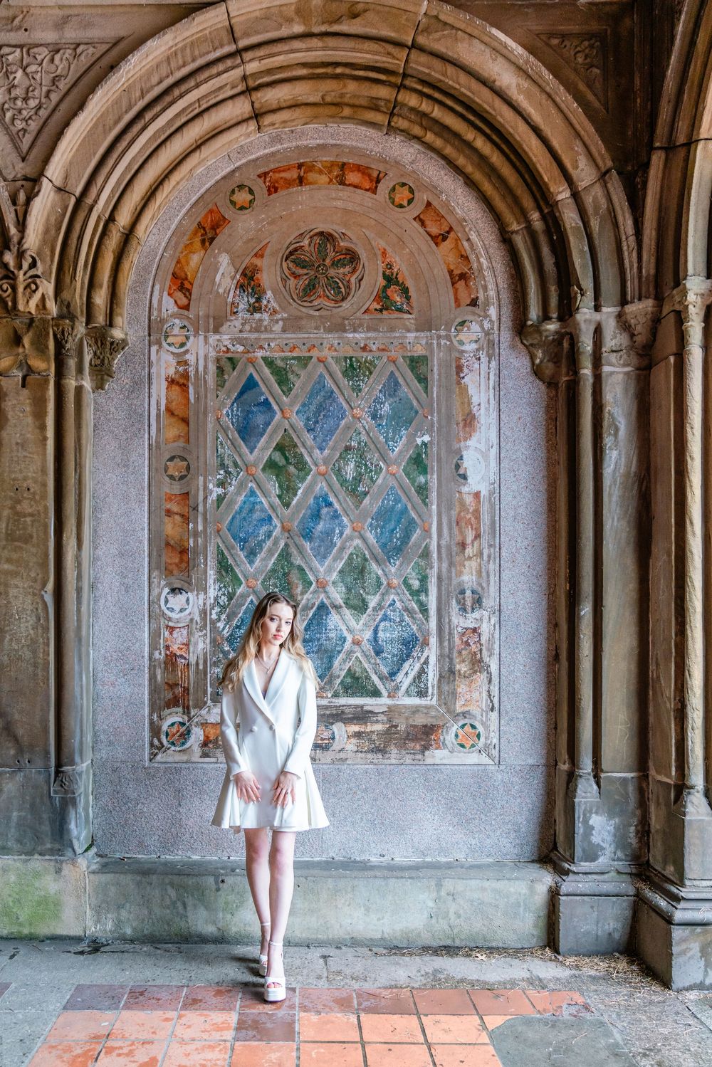 Young woman in white dress standing before ornate arched mosaic window at Bethesda Terrace, Central Park.