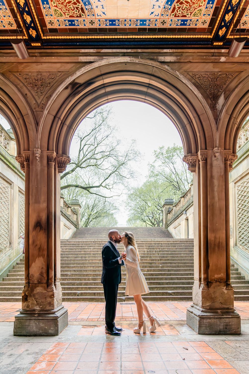 Couple sharing a romantic kiss under the ornate arched terrace of Bethesda Fountain in Central Park, NYC.