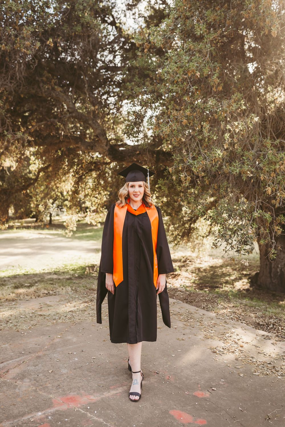 Woman in black graduation gown and cap with orange MSN stole during her photo session with heidi grace photography