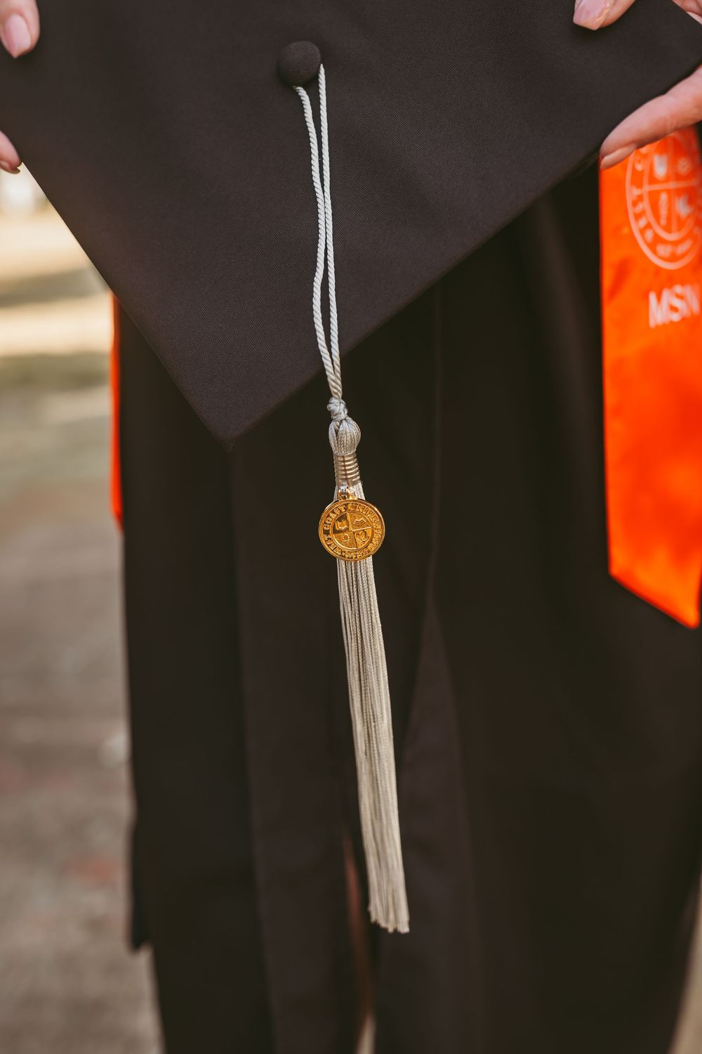 Close-up of a graduation cap tassel with gold medallion pendant against black gown.