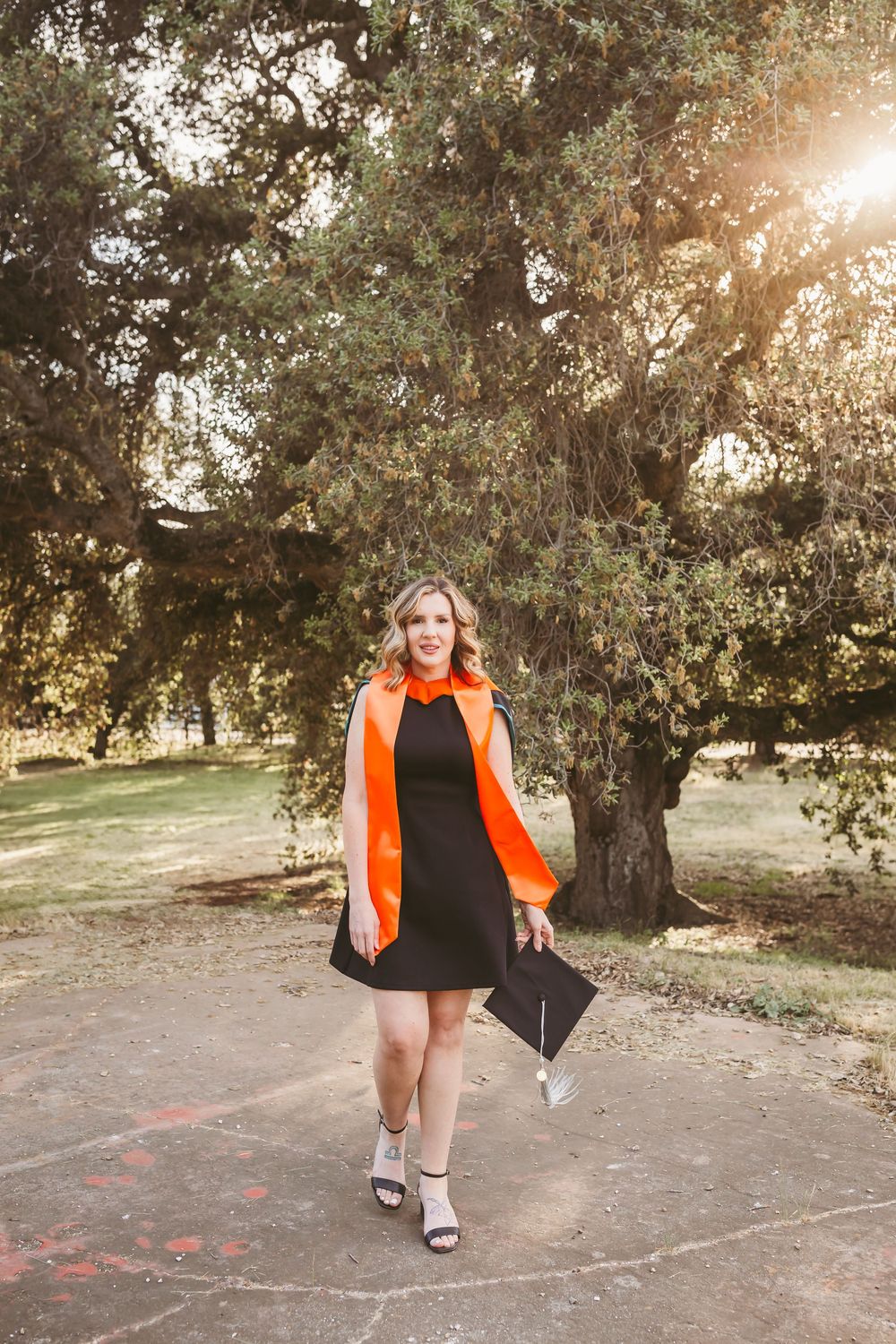 Woman in black dress and orange graduation sash celebrating her masters in nursing with a photo shoot in yucaipa