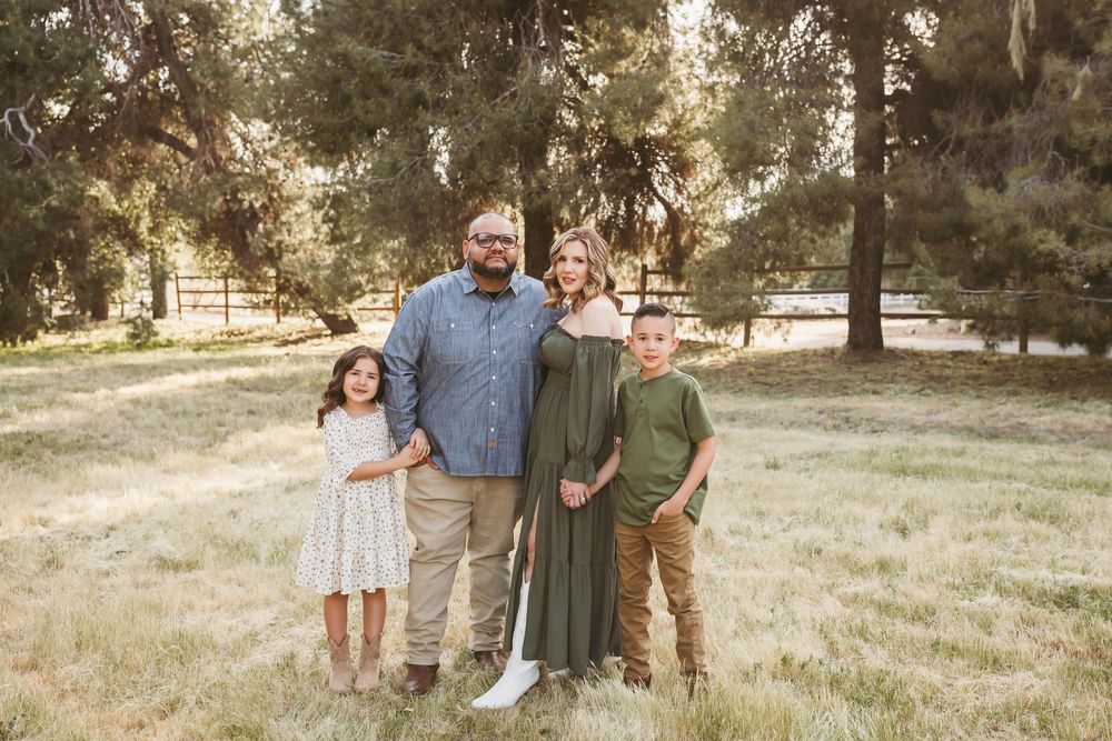 Family of four posing in a sunny park with tall trees, wearing earth tones and green dress in yucaipa ca