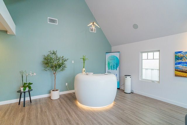 Modern spa reception area with teal accent wall, curved white desk, hardwood floors, and natural light.