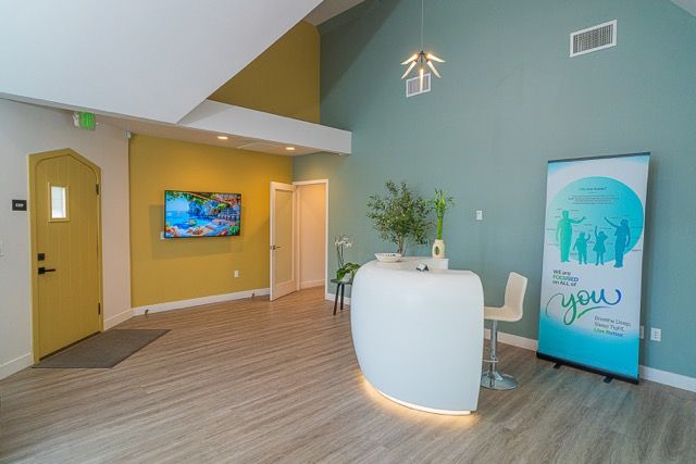 Modern medical office reception area with teal accent wall, white curved desk, yellow door, and welcoming lobby decor.