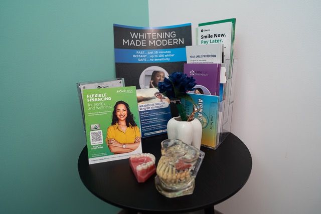 Dental office display table with teeth whitening brochures, smile financing pamphlets, and dental model samples on a black round table.