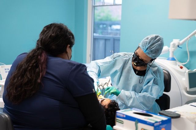 Dentist in surgical gear performing a dental procedure on a patient in a modern teal-colored dental office.