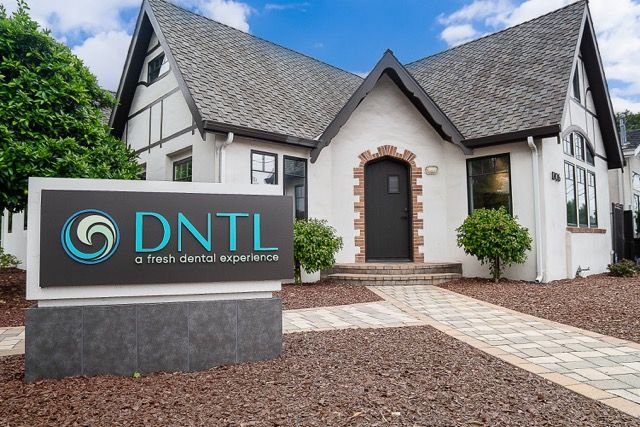 DNTL fresh dental experience office exterior, modern Tudor-style building with stone sign and manicured landscaping.