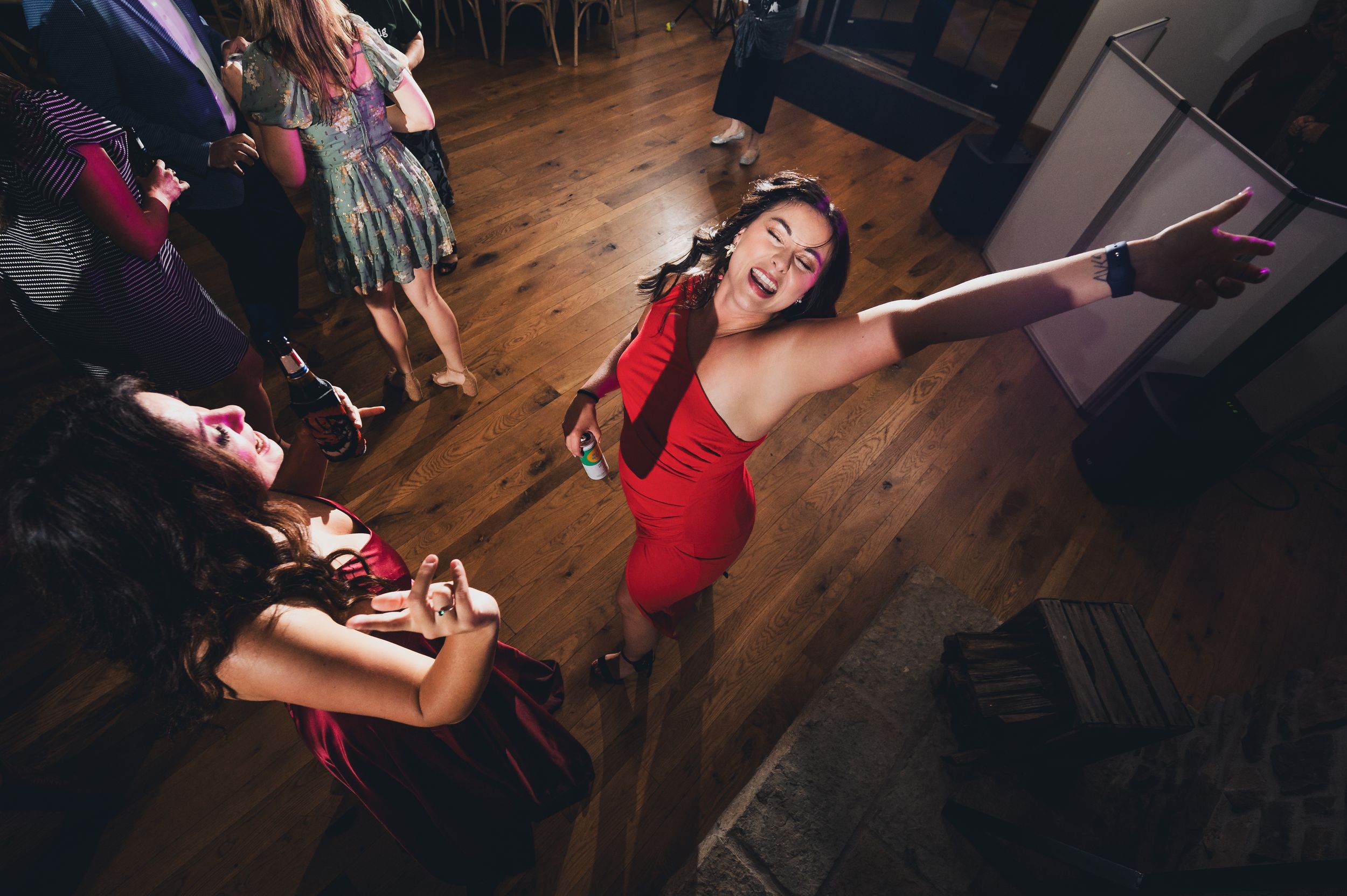 Woman in red dress dancing joyfully at a party on a wooden floor with guests in the background.