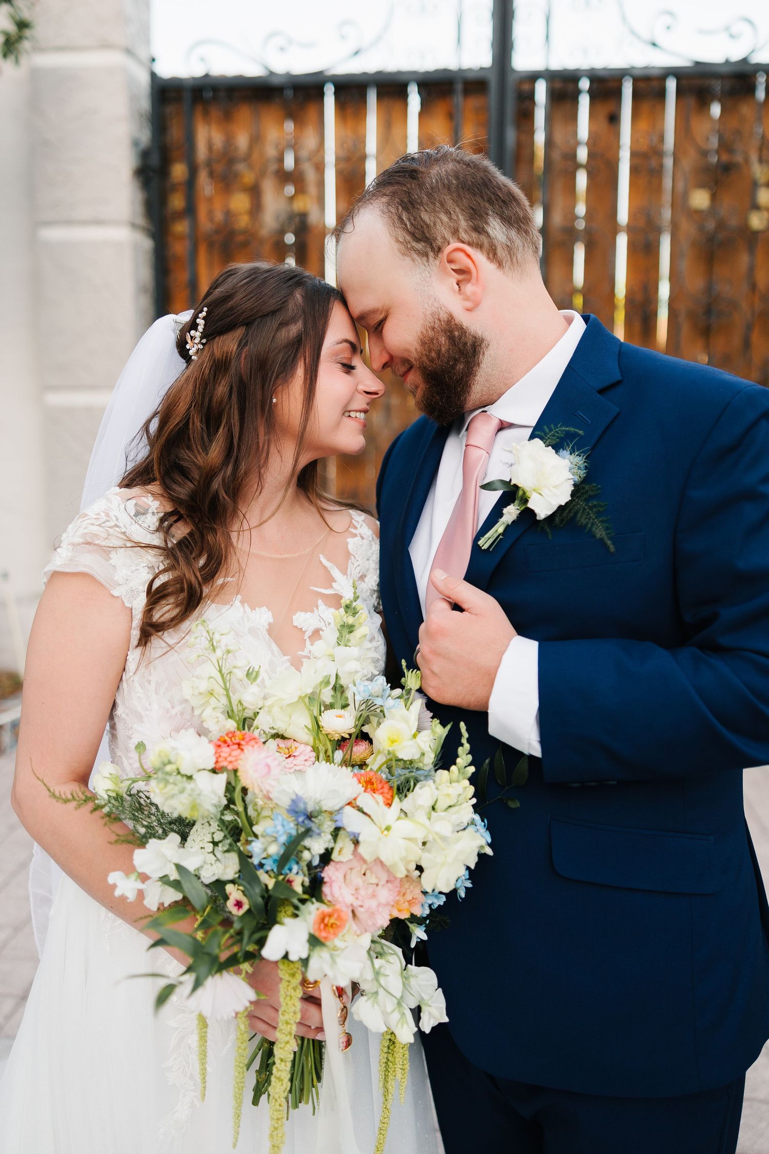 Bride and groom sharing a romantic kiss at golden hour, groom in navy suit with pink tie and white boutonniere.