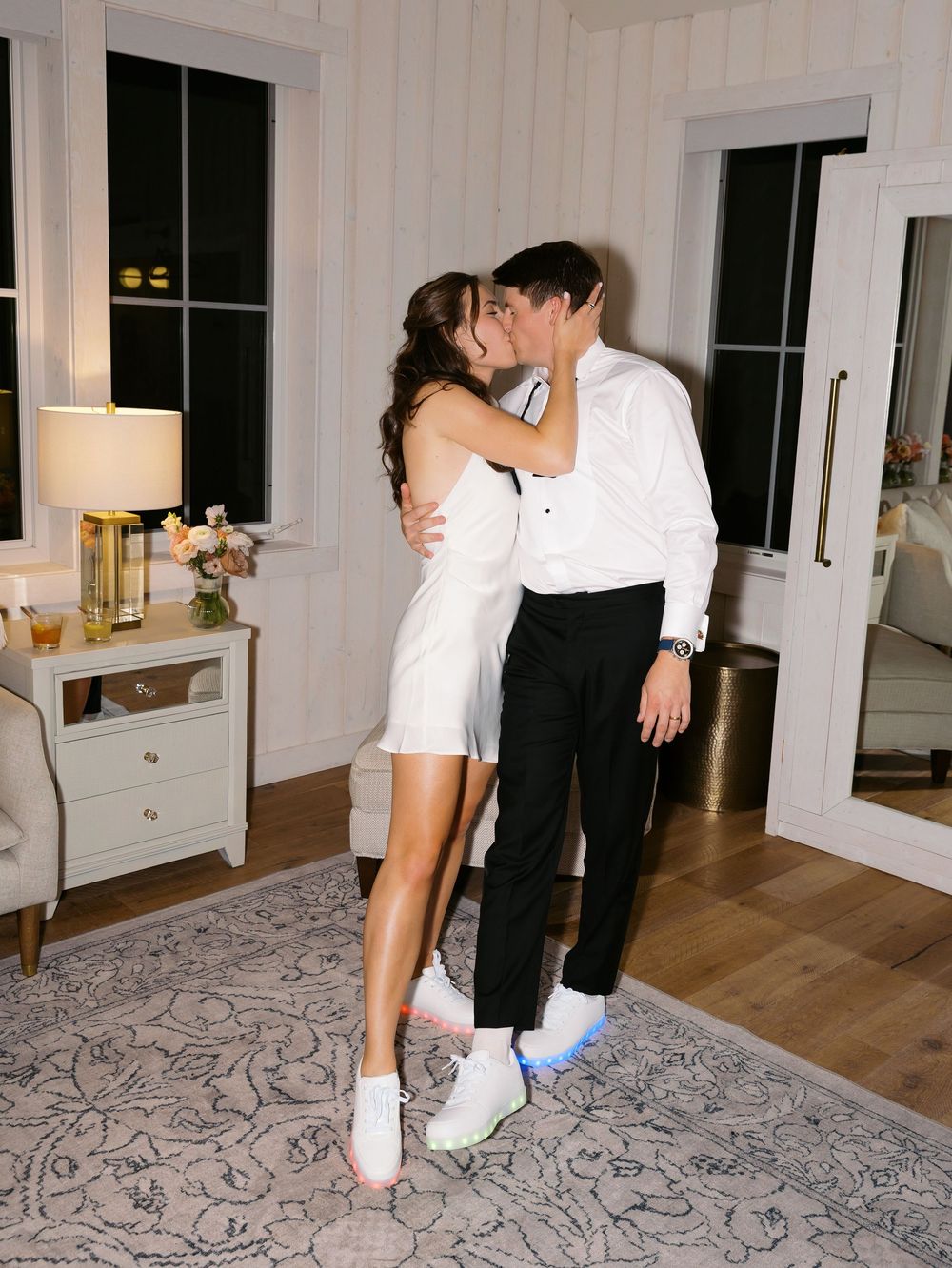 Couple sharing a romantic kiss in elegant white outfits and colorful sneakers during their wedding reception.