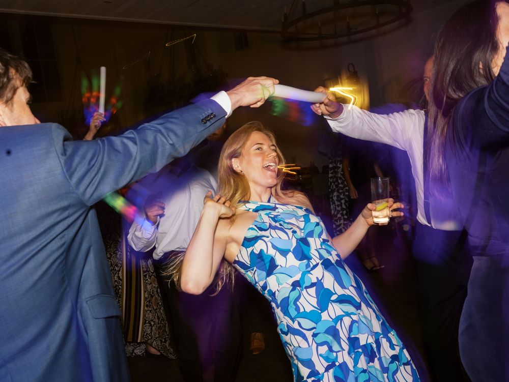 Woman in blue floral dress dancing at a lively party with colorful lights and guests celebrating.