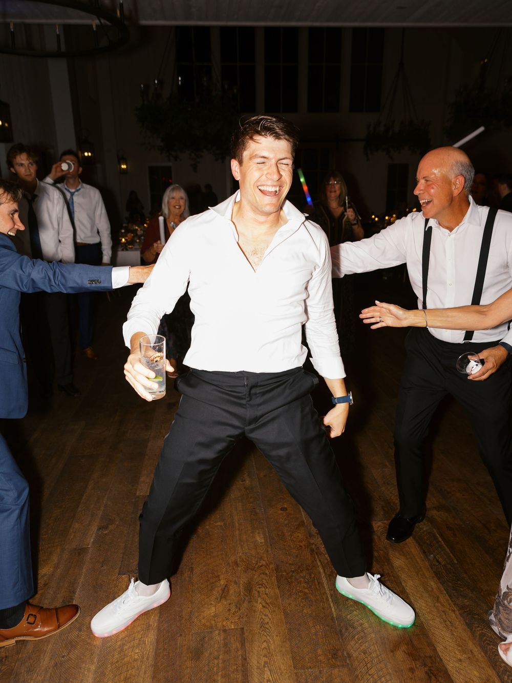 Groom dancing energetically on wedding reception dance floor in white shirt and light-up sneakers.