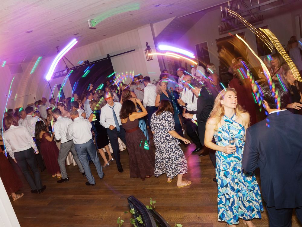 Crowded wedding reception dance floor with colorful neon lights and guests dancing.