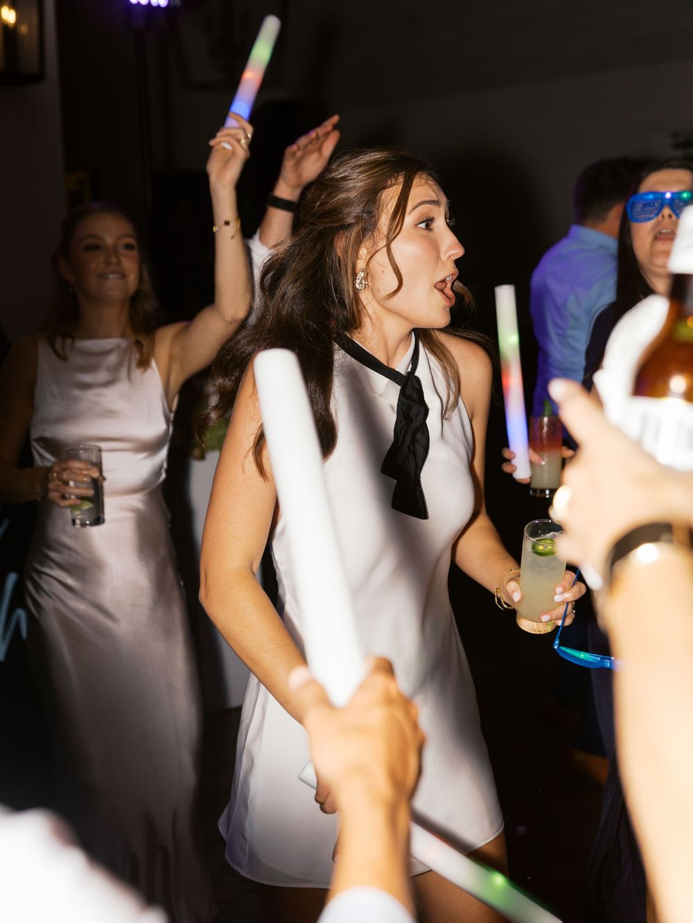 Woman in white dress dancing with glow sticks at a lively wedding reception party.