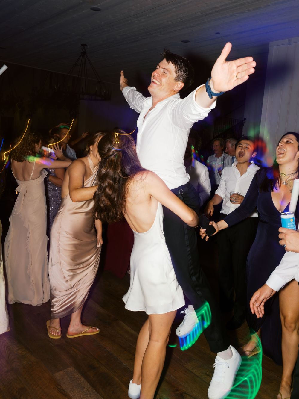 Groom lifting bride in white dress during lively wedding reception dance floor celebration.