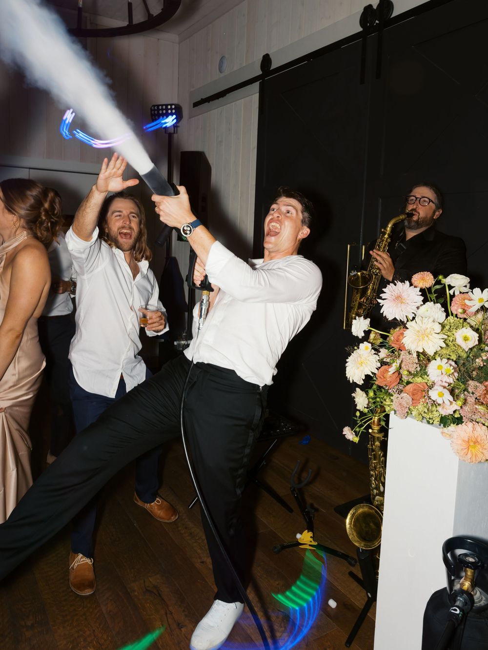 Groom celebrating at wedding reception with confetti cannon while band plays saxophone in background.