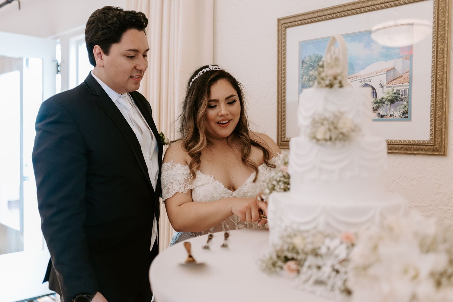 Bride and groom cutting their white wedding cake together at an elegant indoor reception venue called The Thursday Club.