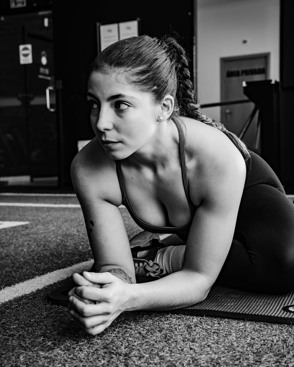 Black and white photo of a fit woman stretching on a gym floor, wearing a sports bra and leggings.