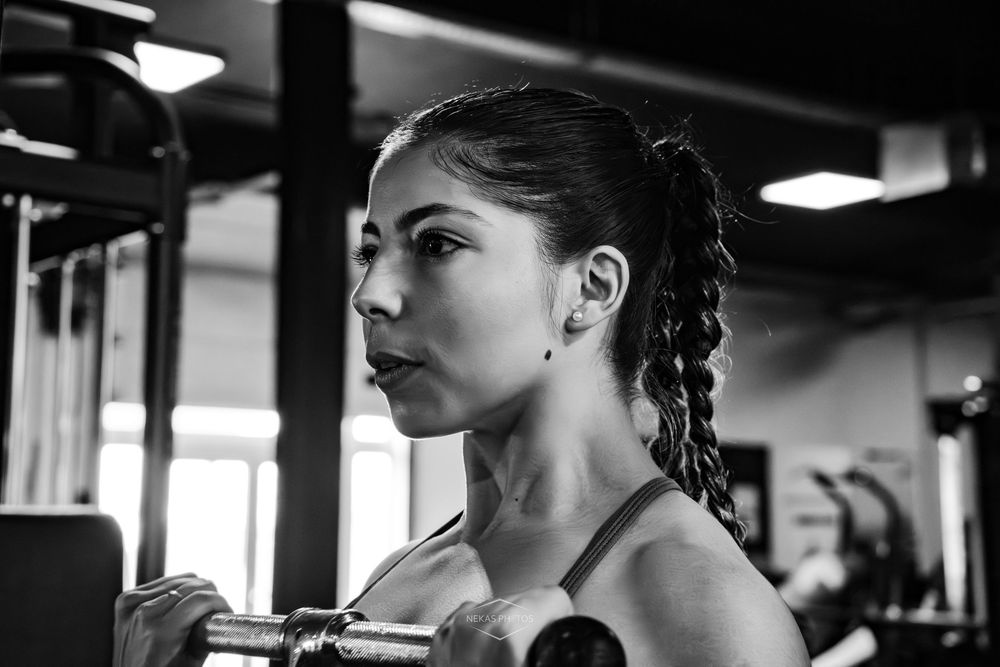 Black and white photo of a focused woman lifting dumbbells during an intense workout session in a gym.