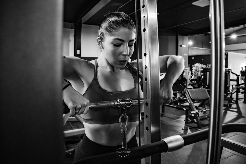 Woman lifting barbell in gym, black and white fitness photography showcasing strength training workout.