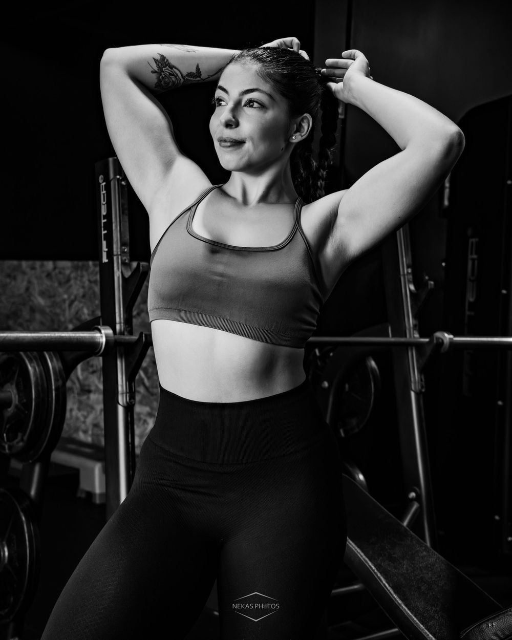 Black and white gym photo of a fit woman in sports bra and leggings posing confidently with hands behind her head.