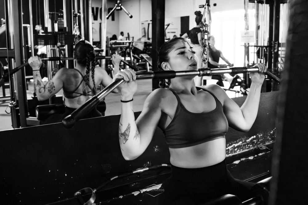Woman performing pull-ups on a bar in a gym, captured in black and white photography.