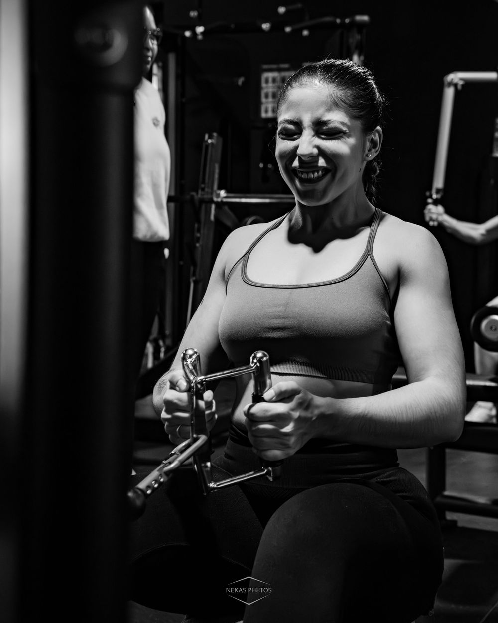 Woman laughing while using cable machine at gym, black and white fitness photography.
