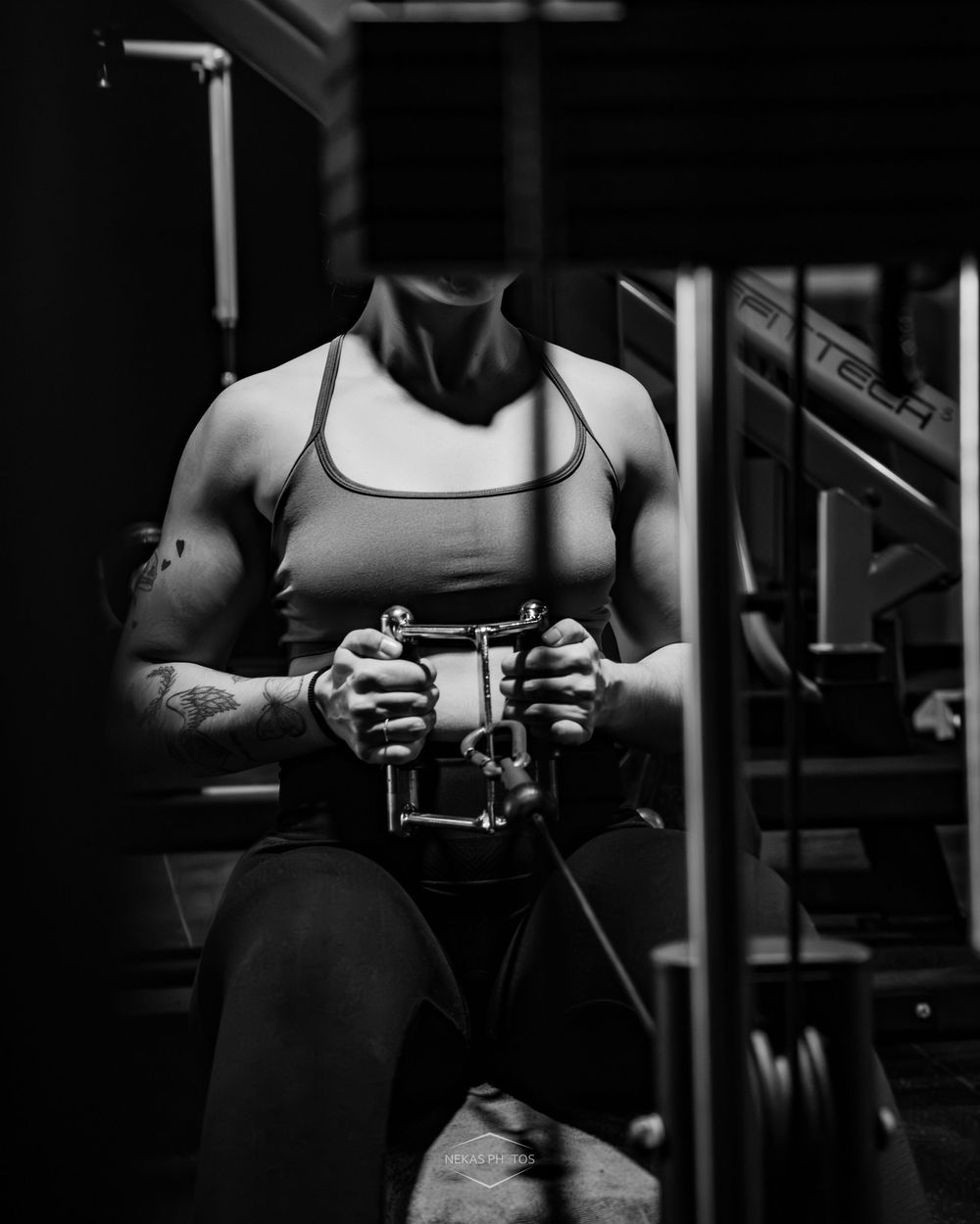 Black and white photo of a muscular person doing cable rows on a gym machine, showcasing strength and fitness.
