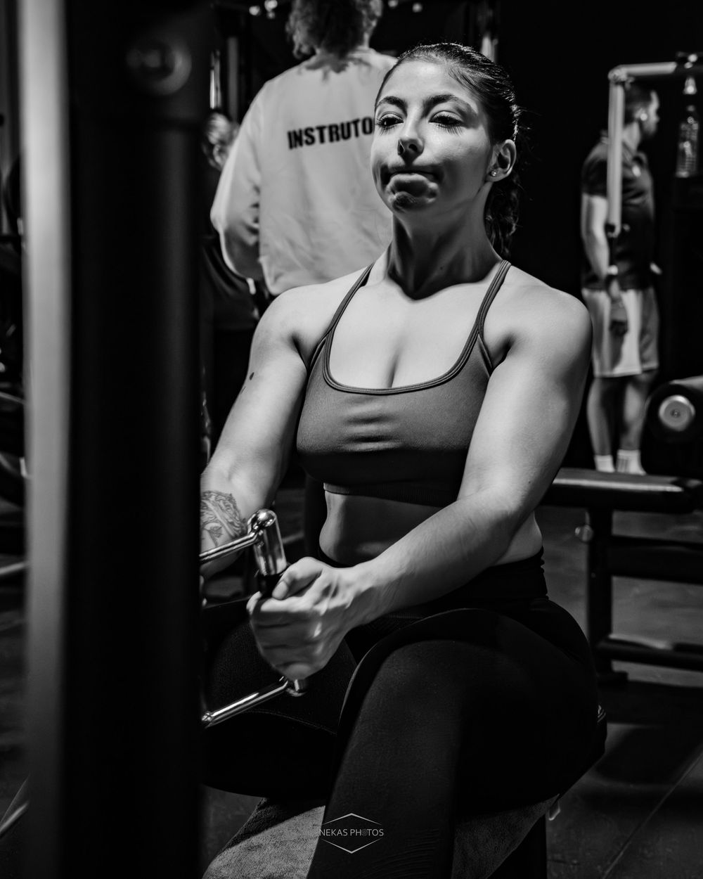 Woman lifting dumbbells in gym wearing sports bra, black and white fitness photography.
