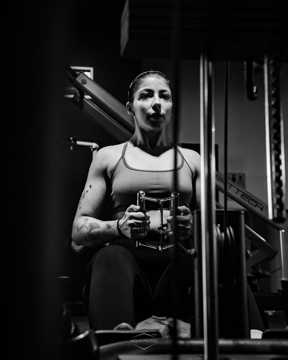 Black and white photo of a woman working out on a cable machine in a gym, wearing athletic wear.