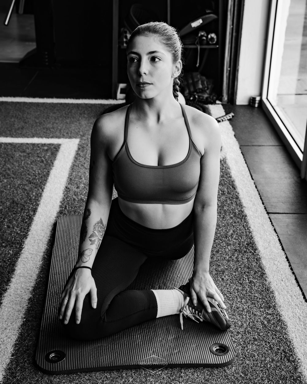 Woman in sports bra and leggings stretching on yoga mat in gym, black and white fitness photo.