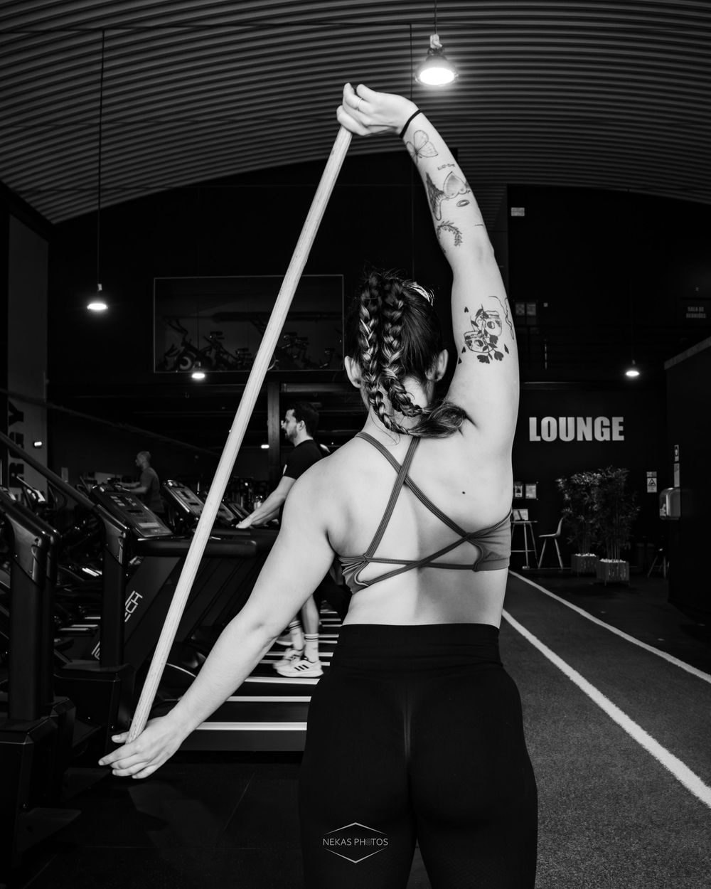 Woman with tattoos and braids exercises with resistance band in black and white gym photo.
