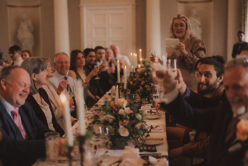 Guests raising glasses in a toast at an elegant candlelit wedding reception dinner along a long decorated table.
