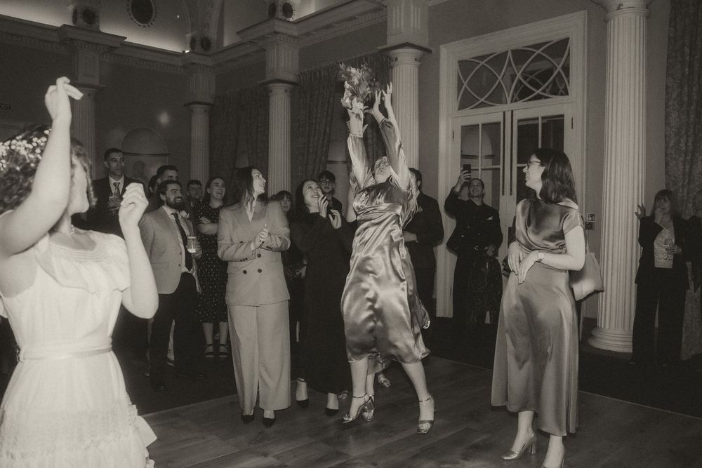 Black and white photo of women catching a bouquet at a wedding reception on a dance floor.