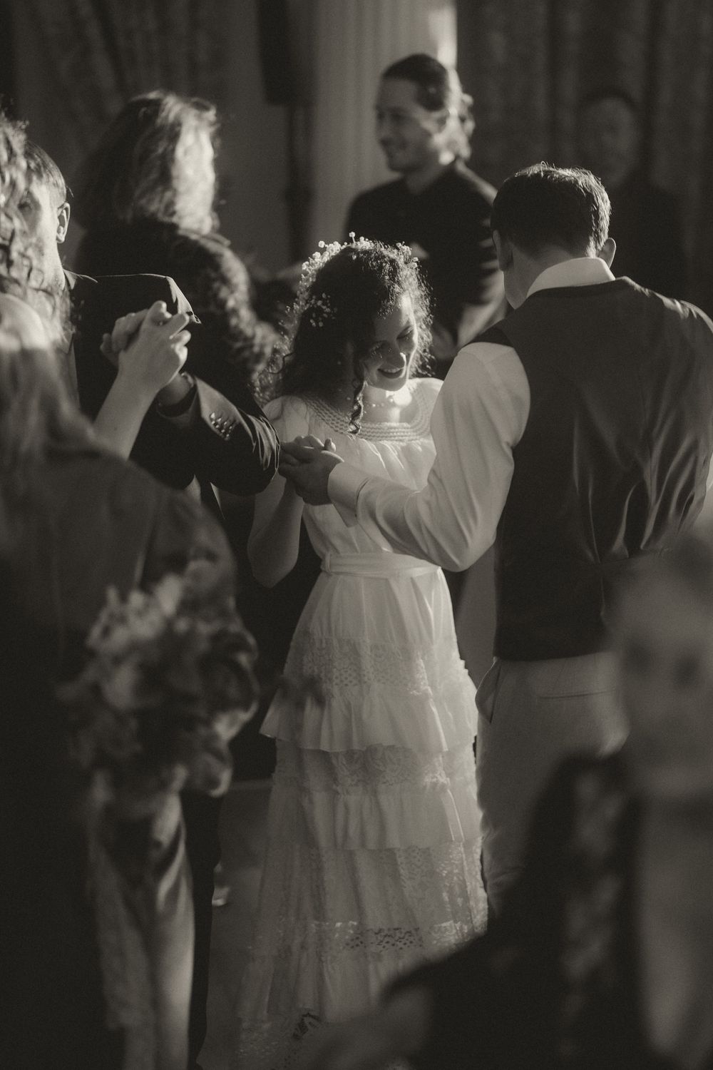 Black and white photo of a young flower girl in a white dress dancing with a man at a wedding reception.