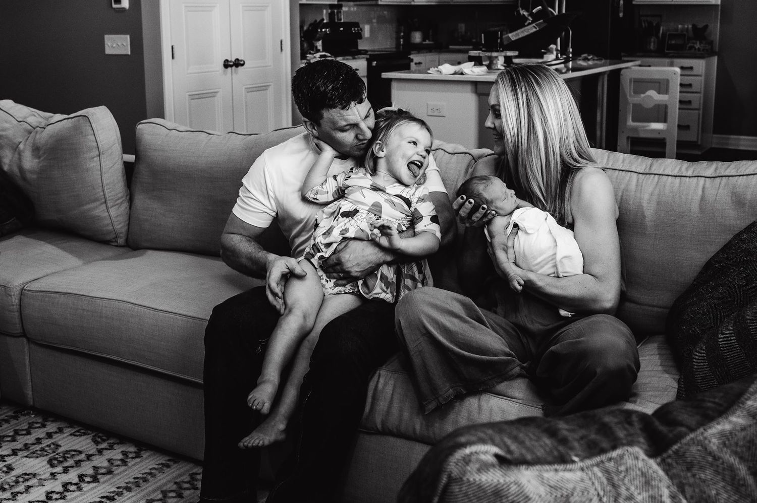 Family sitting together on gray couch sharing intimate moment with newborn.