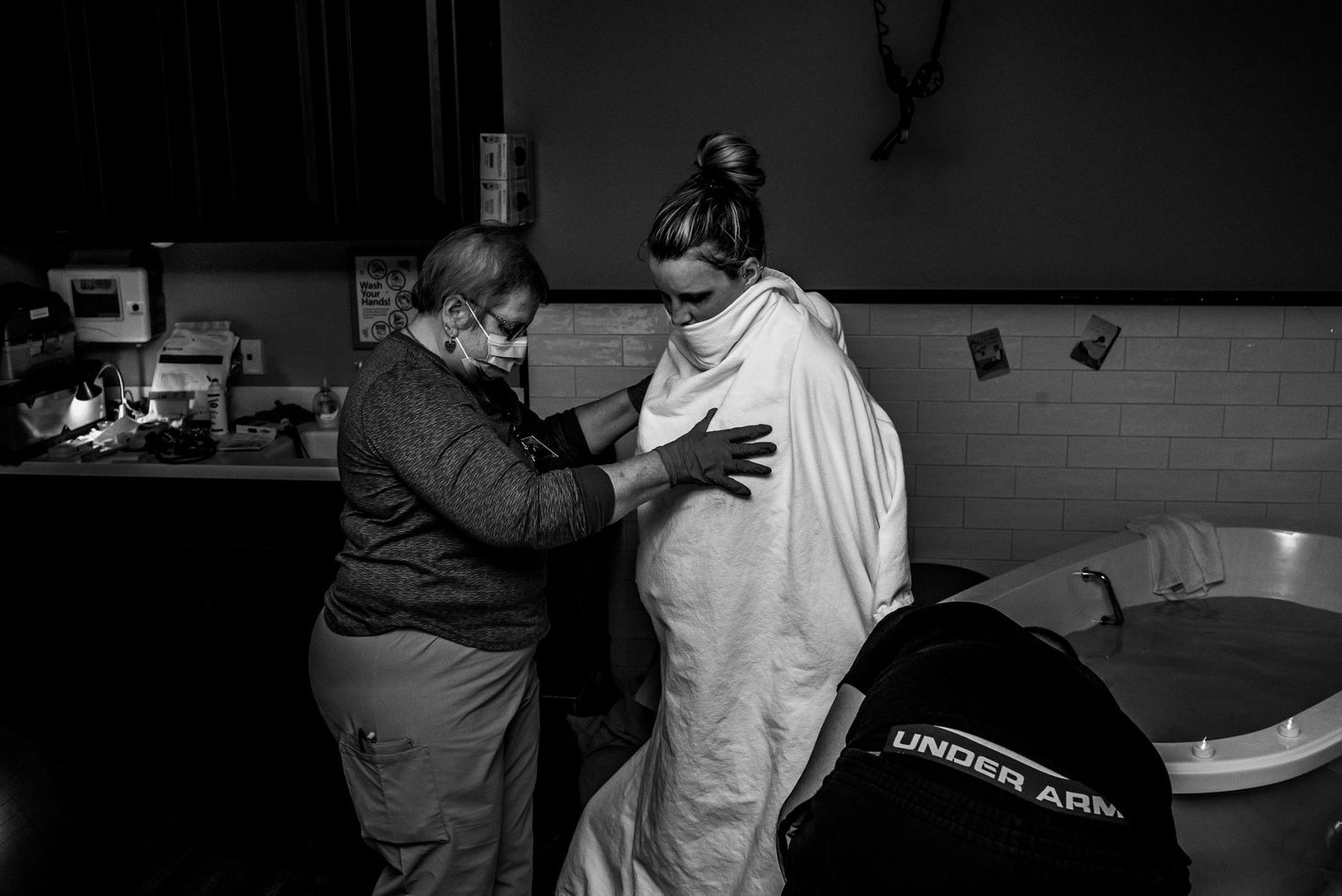 A support person provides comfort measures to a mother in labor in a dimly lit room.