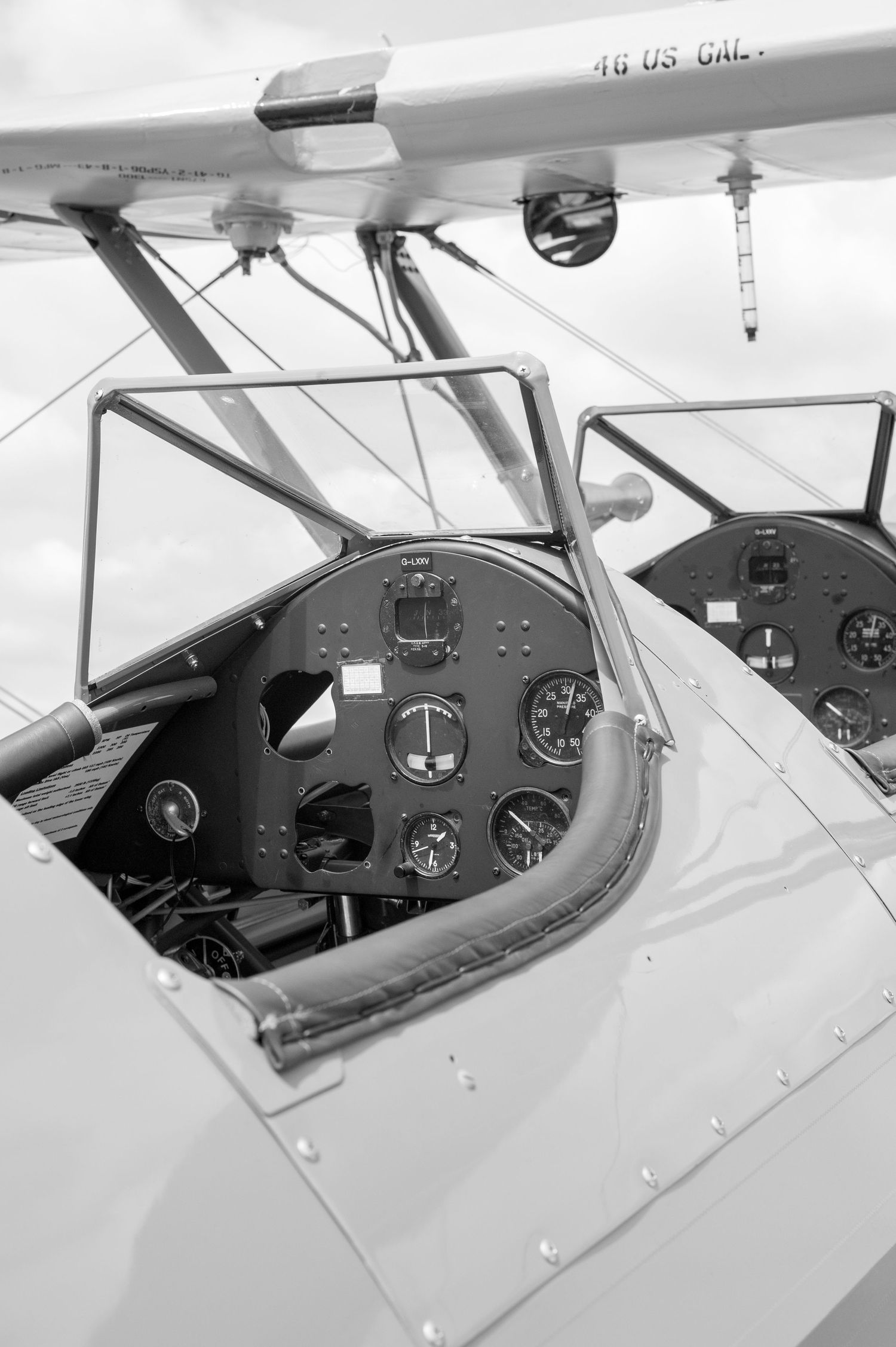 Black and white close-up of a vintage biplane cockpit showing dual instrument panels and open-air design.