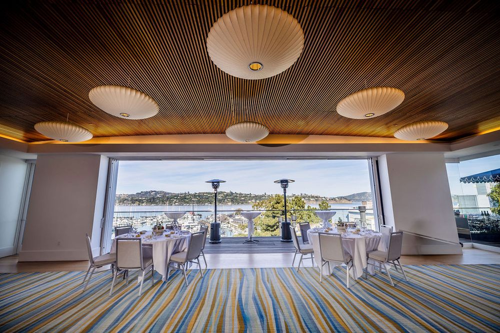 Elegant banquet room with ocean view, striped carpet, round tables, and modern pendant lights on wood ceiling.