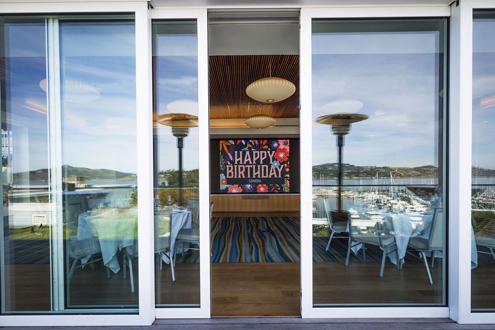 Outdoor patio with sliding glass doors, patio heaters, dining tables, and a Happy Birthday banner inside.