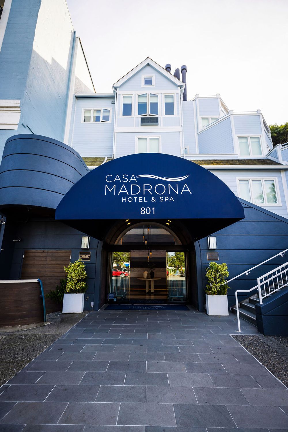 Casa Madrona Hotel & Spa entrance at 801, featuring a navy blue awning and elegant stone pathway.