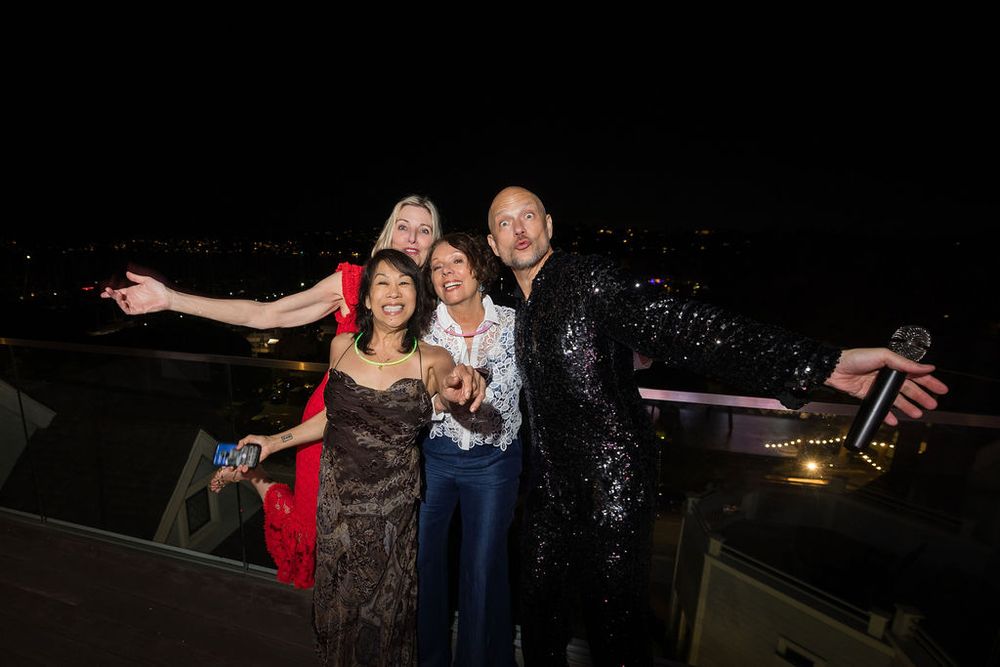 Four friends pose and smile together at a glamorous nighttime rooftop party event.