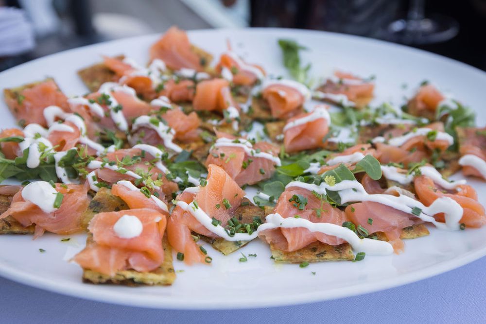 Smoked salmon appetizers on crispy crackers topped with cream cheese drizzle and fresh herbs on a white plate.