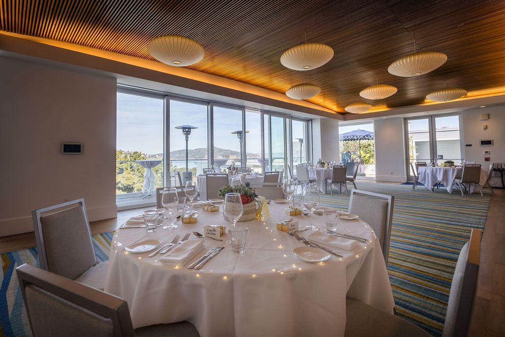 Elegant banquet hall with round tables, white linens, and panoramic ocean views through floor-to-ceiling windows.