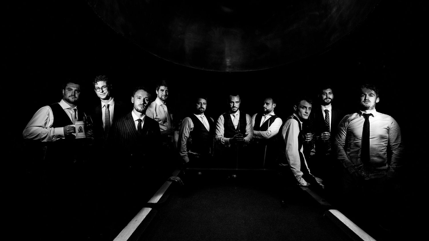 Black and white group photo of a formal music ensemble posing dramatically in dim stage lighting.