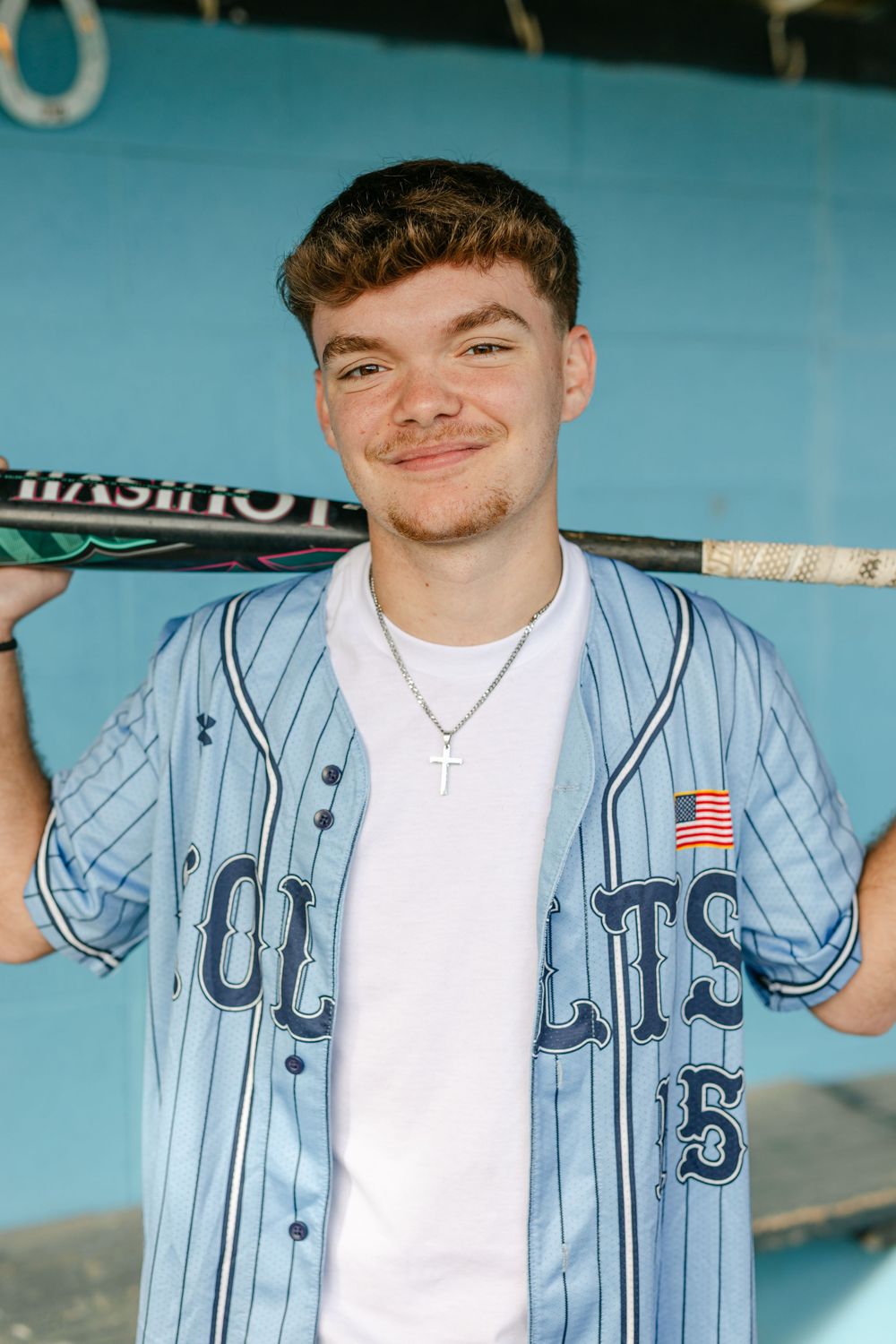 Young male baseball player in Colts pinstripe jersey smiling while holding bat behind his shoulders.