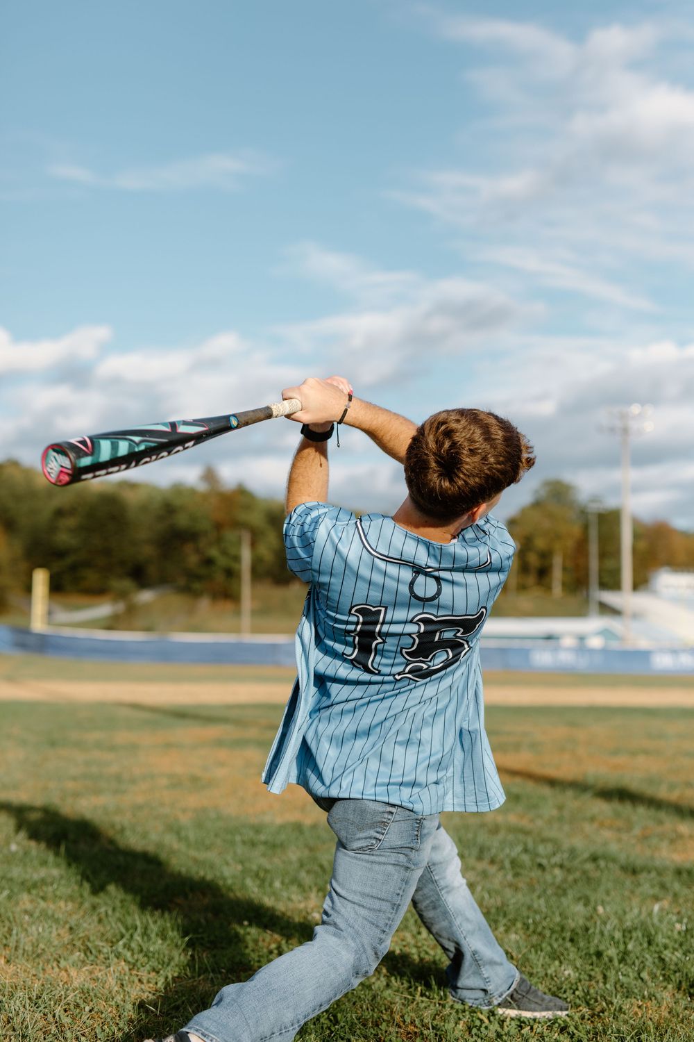 Young baseball player in blue pinstripe number 15 jersey following through on bat swing outdoors.