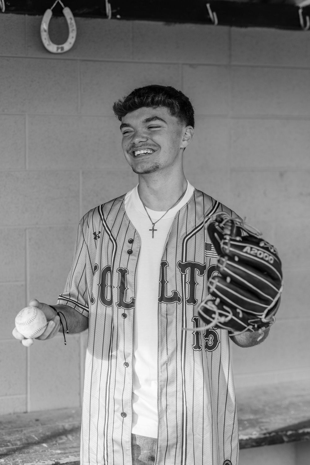 Smiling baseball player in pinstripe jersey holding ball and glove in black and white photo.