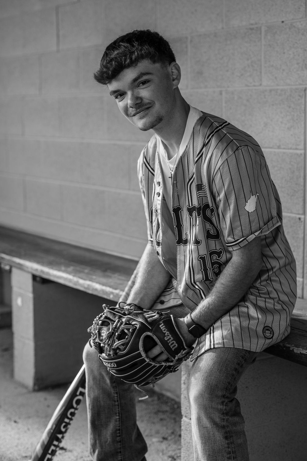 Smiling baseball player sitting on dugout bench with glove in black and white portrait.